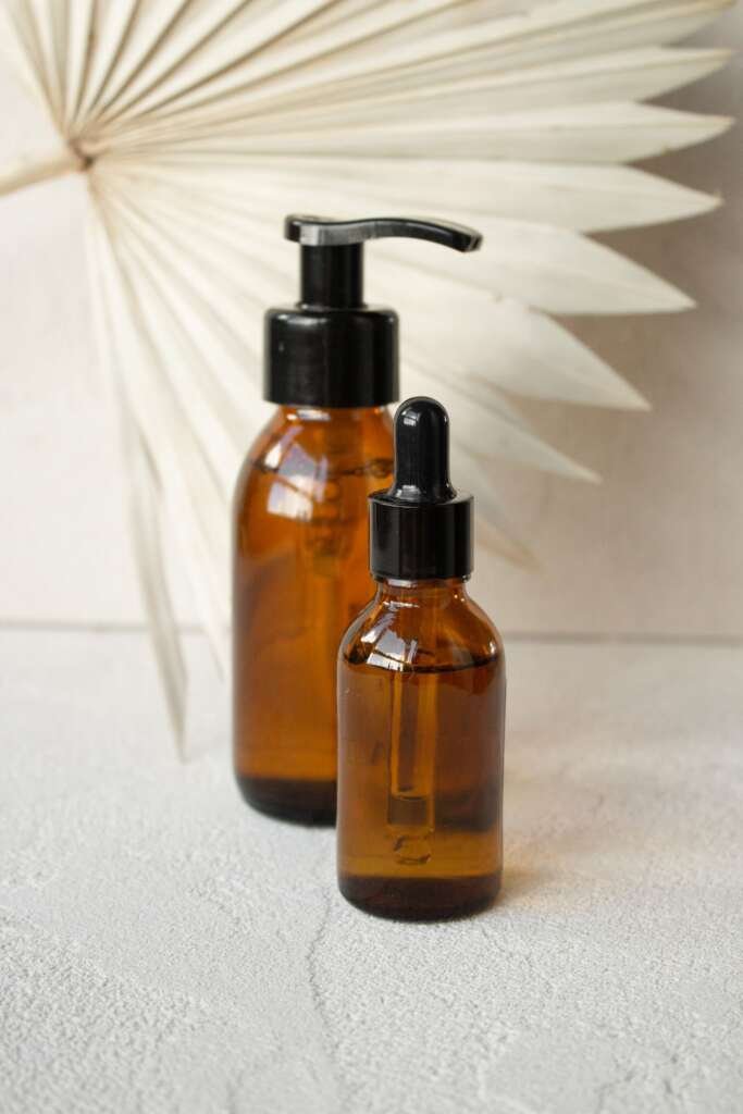 Amber pump and dropper bottles on a cream surface with a dried palm fan